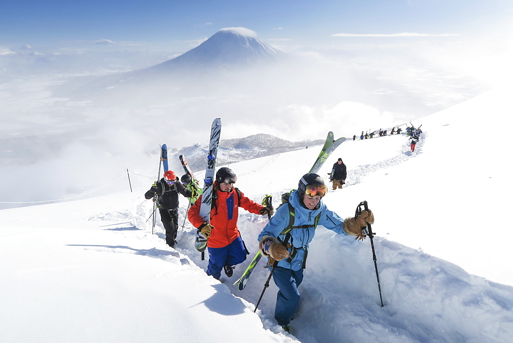 With Mount Yotei in the background, a team of backcountry skiers, led by a woman, are hiking to the summit of mount Annupuri, near ski resort Niseko United on the Japanese island of Hokkaido. The skis they carry are big and wide allowing the winter enthusiasts to fully enjoy skiing down the waist deep powder slopes Niseko United is known for. Niseko United is comprised of four resorts on the one mountain, Annupuri (1,308m). 100km south of Sapporo, Niseko Annupuri is a part of the Niseko-Shakotan-Otaru Kaigan Quasi-National Park and is the most eastern park of the Niseko Volcanic Group. Hokkaido, the north island of Japan, is geographically ideally located in the path of consistent weather systems that bring the cold air across the Sea of Japan from Siberia. This results in many of the resorts being absolutely dumped with powder that is renowned for being incredibly dry. Some of the Hokkaido ski resorts receive an amazing average of 14-18 meters of snowfall annually. Niseko is the powder capital of the world and as such is the most popular international ski destination in Japan. It offers an unforgettable experience for all levels of skier and snowboarder.