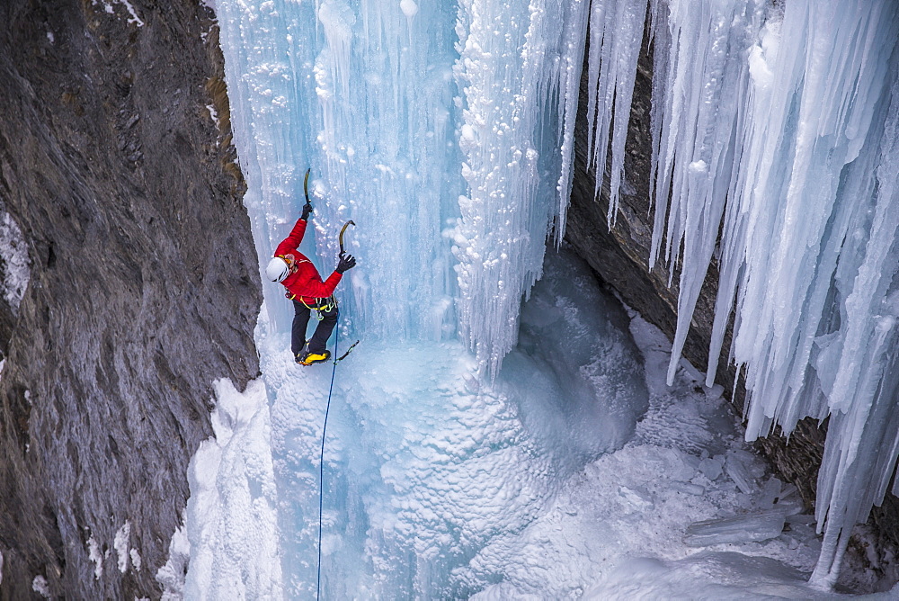 A man in a red jacket is climbing on ice.