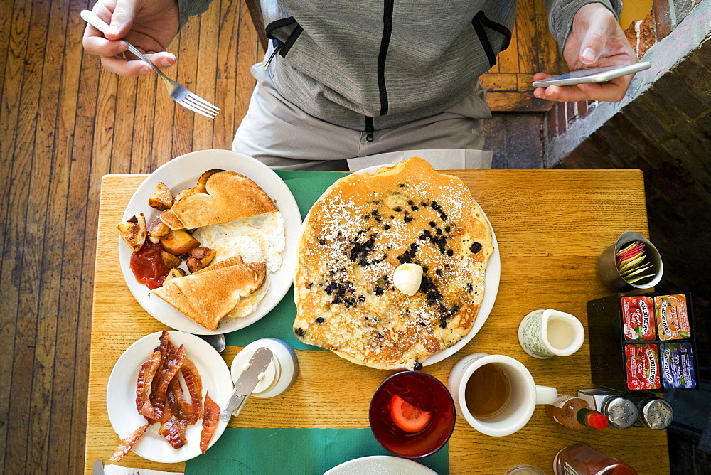 Man sitting in front of breakfast food at a restaurant, using smartphone