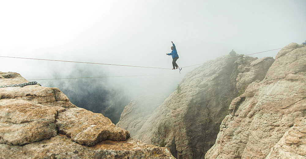 Man Walking On Slackline In Fog Over A Canyon