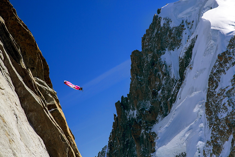 Person Flying In A Bright Red-and-white Wingsuit Between Two Mountains