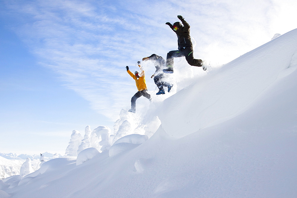 Three Men Jumping Off A Snow Cornice Near Whitefish, Montana, Usa