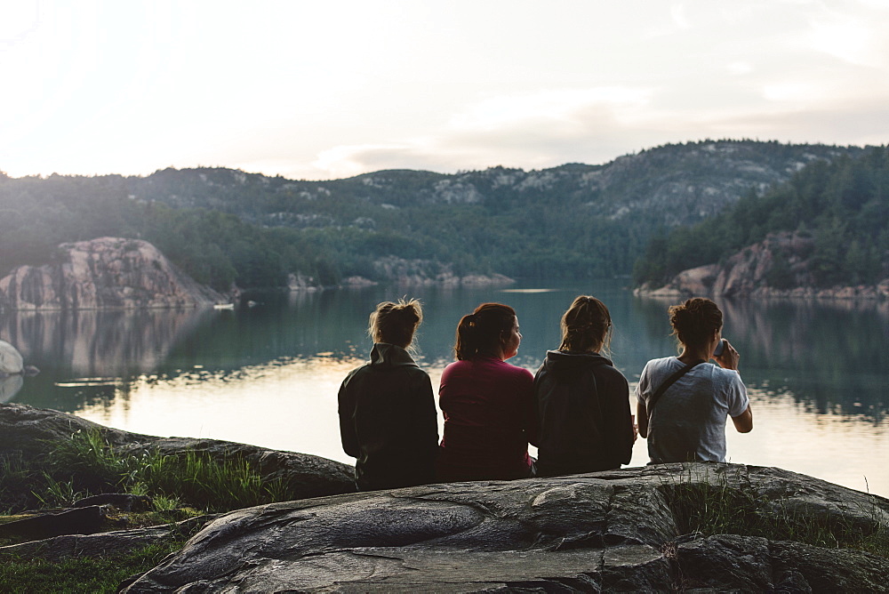 Four Young Women Are Sitting And Relaxing By The Lake At Dusk