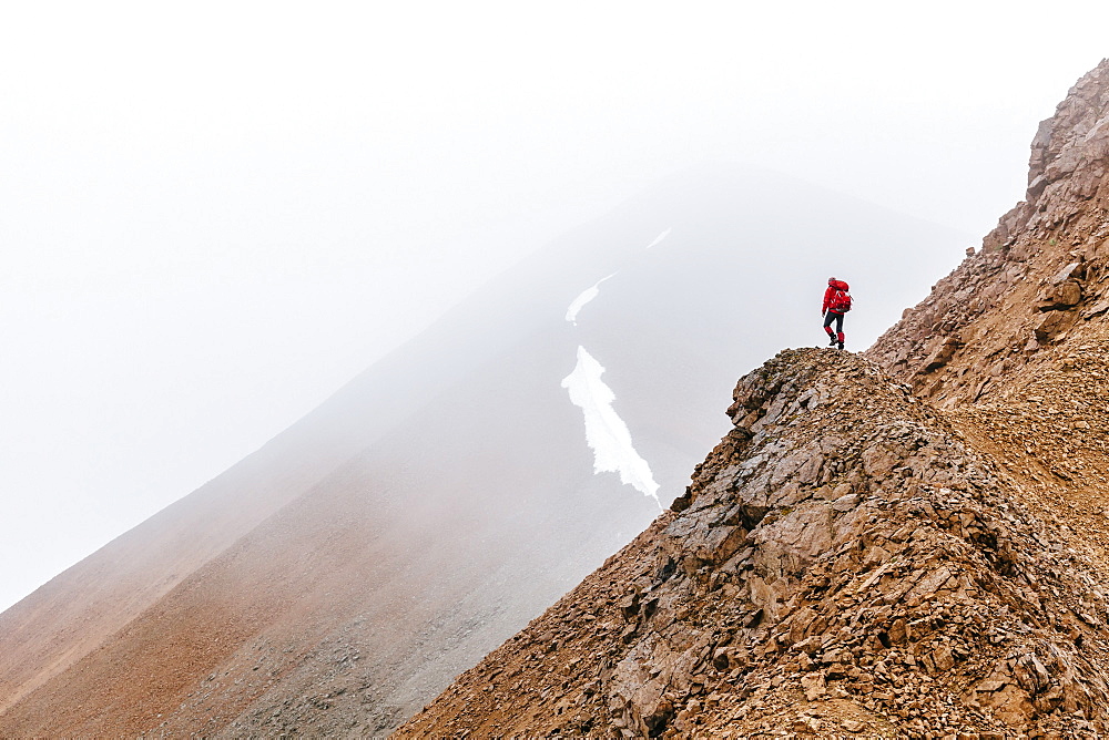 A Woman Is Hiking On A Ridge In Fog In The Delta Mountains, Alaska Range, Alaska, Usa