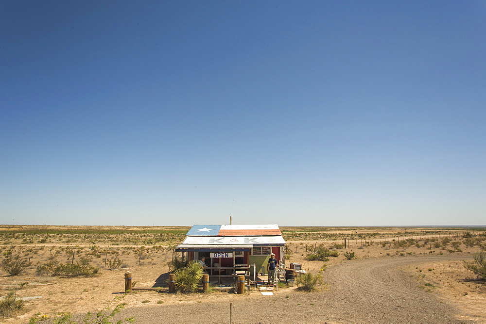 A Solitary Roadside Shack With The Texas Flag Painted On The Roof On An Empty Desert Landscape