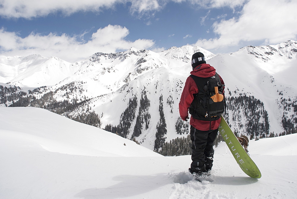 Man Standing With His Snowboard Looking Over Avalanche Paths At Silverton Mountain