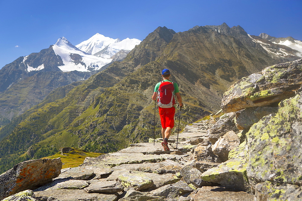 A Hiker Walking Over A Rocky Historical Trade Road With The Weisshorn Towering Above The Matterhorn Valley