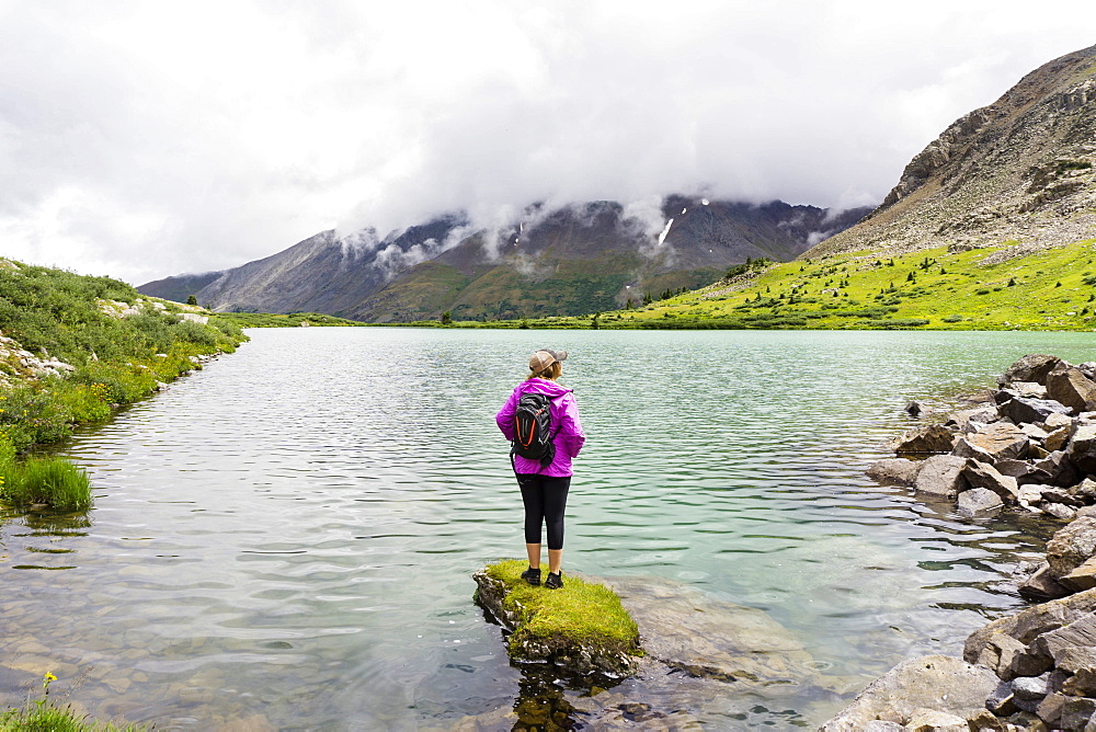 Young female stands on rock in a high alpine lake in Colorado