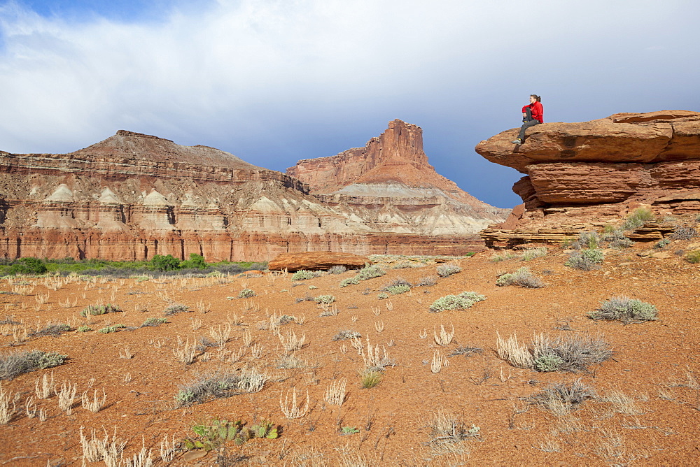 A woman sits on a bedrock terrace at Saddle Horse Bottom below tall canyon walls in Canyonlands National Park, Utah.