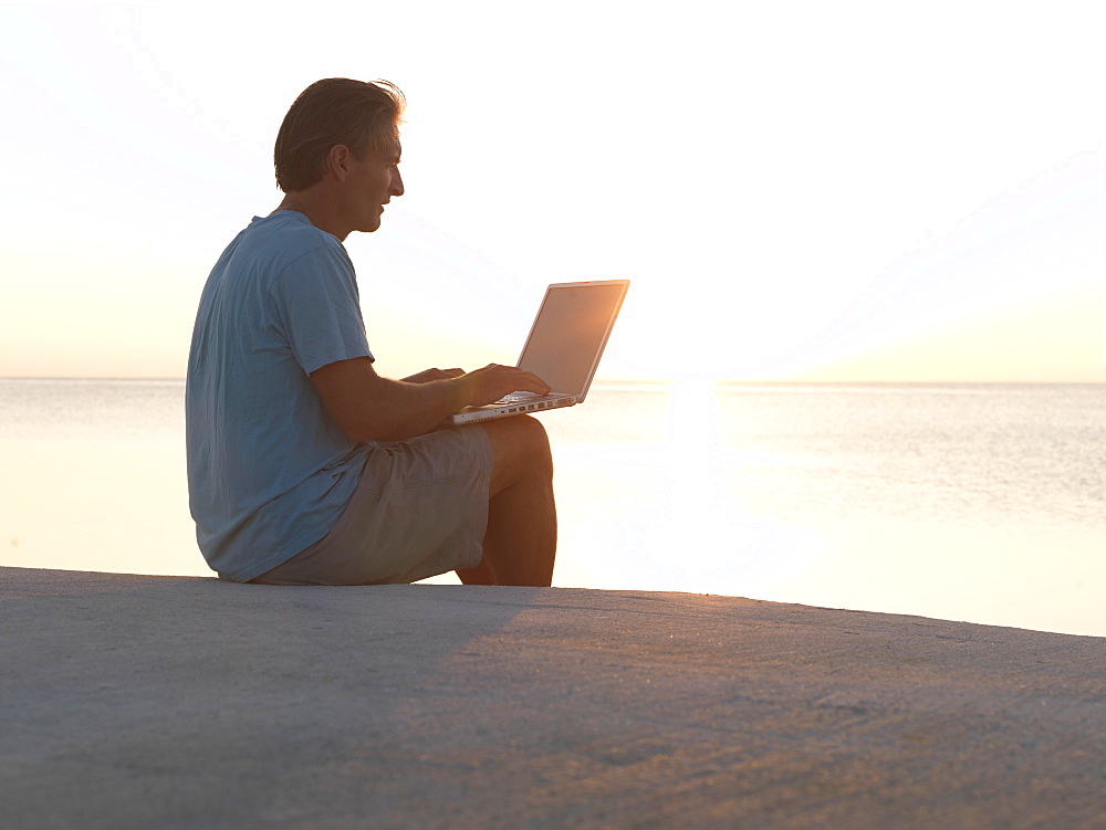 Man uses laptop computer on beach at sunset