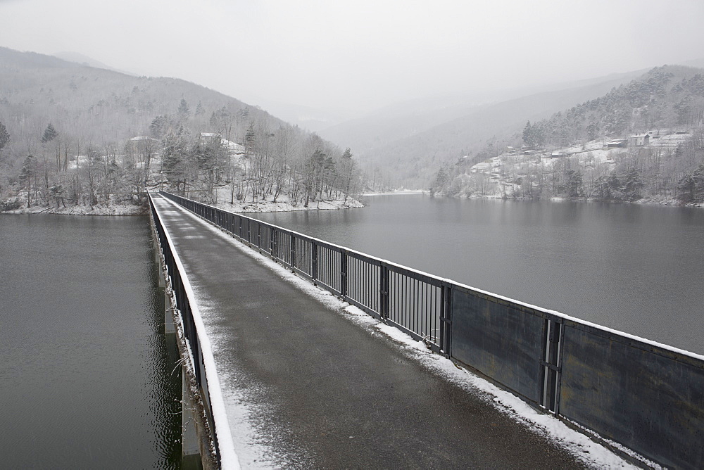 One lane bridge span mountain lake, distant hills and storm