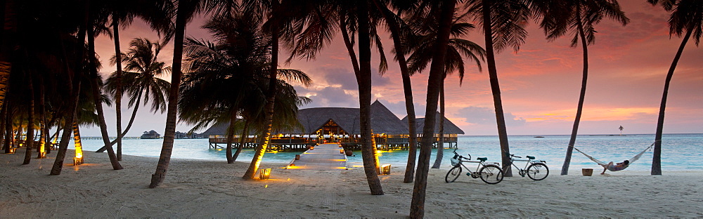 Stilt restaurant in sea behind palm trees at Gili Lankanfushi island at sunset