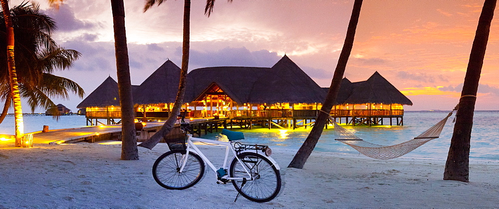 Stilt restaurant in sea behind palm trees at Gili Lankanfushi island at sunset