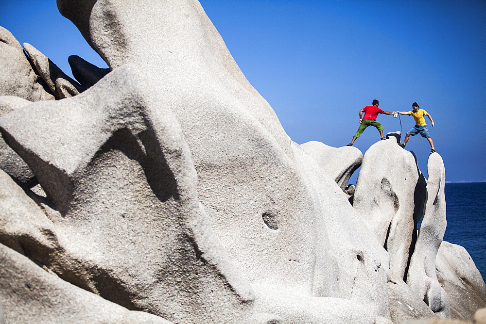 Men climbing on rock near sea, Capo Testa, Sardinia, Italy