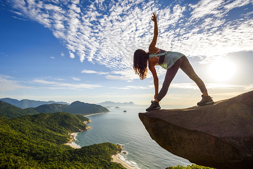 Woman in yoga posture on the edge of the mountain in Pedra do Telégrafo, Barra de Guaratiba, west side of Rio de Janeiro, Brazil