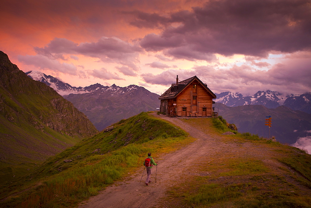 A hiker is almost at the Cabane du Mont Fort, a mountain hut near Verbier. The sunset puts the sky in pink and purple colors. It rained all day, and cleared just before this picture. The hut is one of the places hikers stay at during the Haute Route, a classic hike between Chamonix in France and Zermatt in Switzerland.