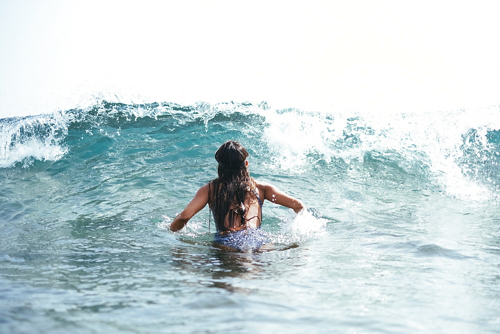 girl in a swimsuit and diving googles playing with the waves on the beach