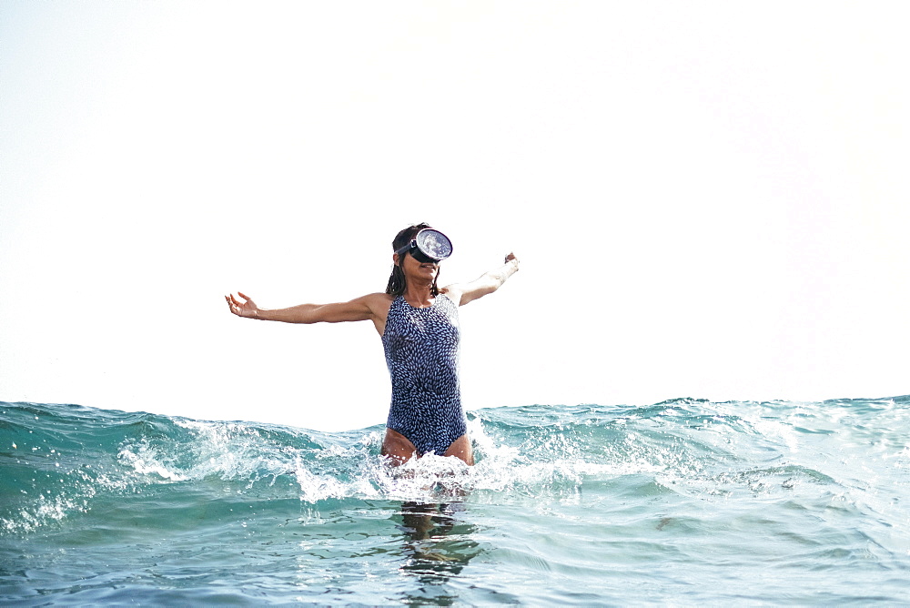 girl in a swimsuit and diving googles playing with the waves on the beach