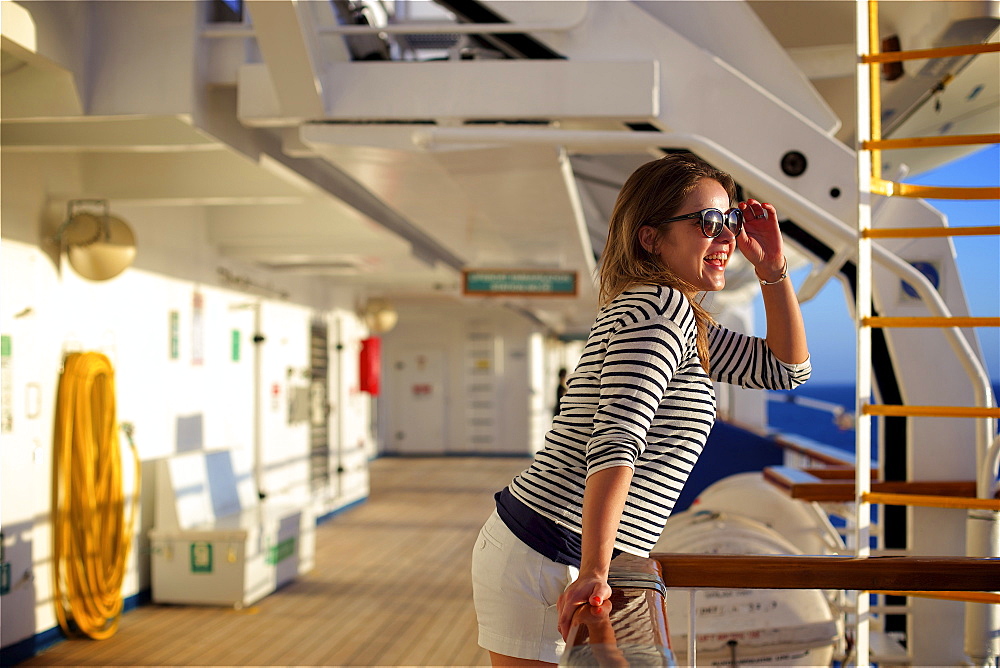 A young woman leans over the railing on the deck of a cruise ship