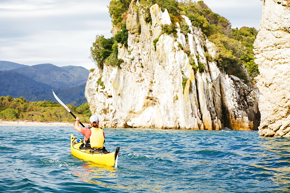 A woman is sea kayaking the coastline of Abel Tasman National Park