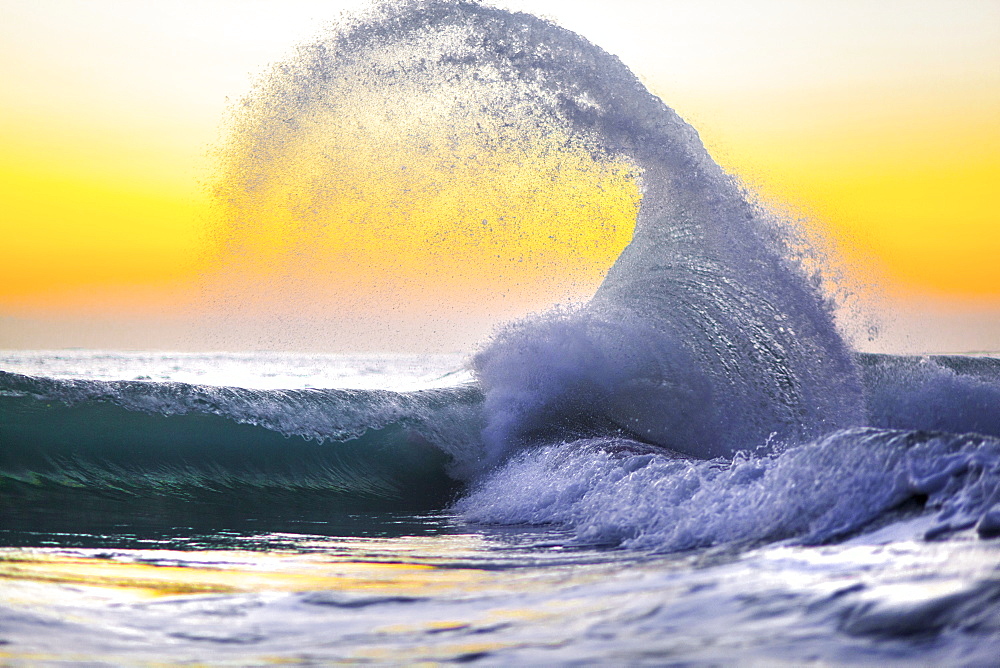 A collision of waves captured againnst a lemon yellow sunrise in Hawaii.