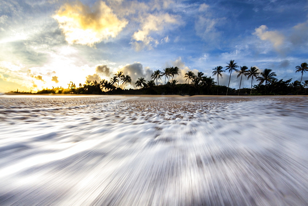 A time lapse of a wave rushing back down the beach on the north shore of oahu, during sunrise.