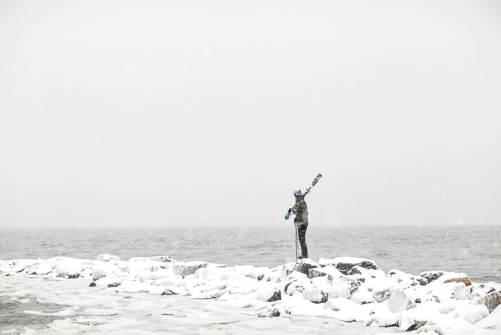 A lone skier stands and looks out at the stormy Atlantic Ocean in Portland, Maine.