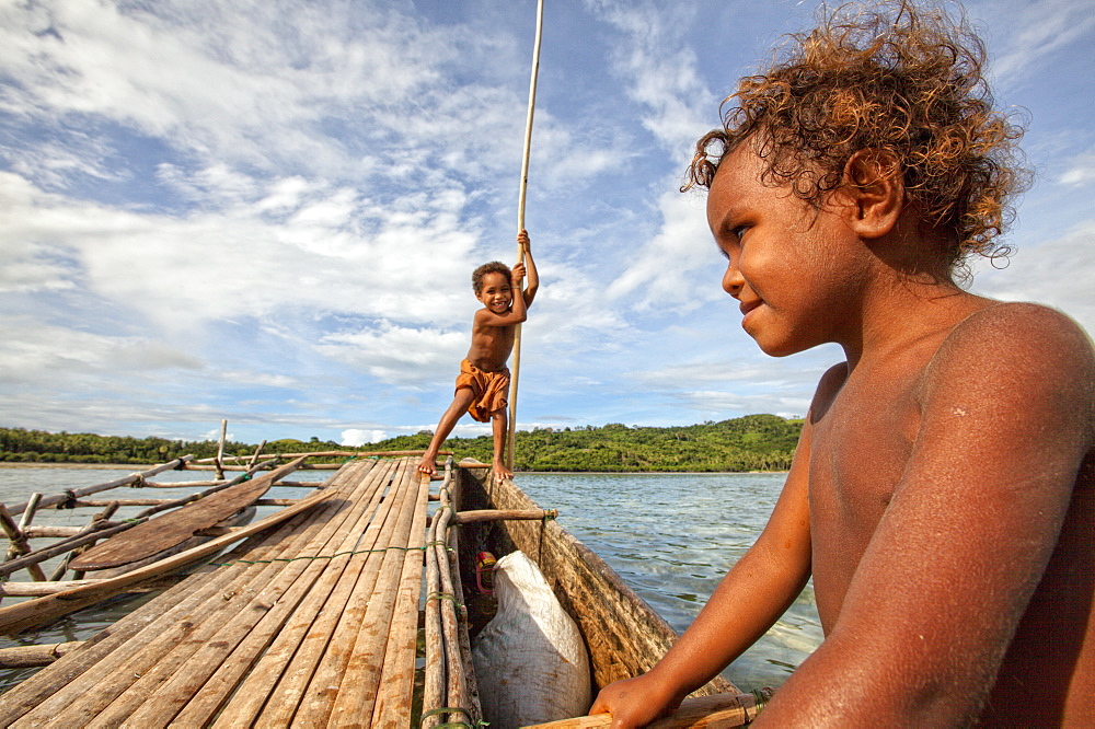 Children playing with a outrigger canoe in the village of Hessessai Bay at PanaTinai (Panatinane)island in the Louisiade Archipelago in Milne Bay Province, Papua New Guinea.  The island has an area of 78 km2. The Louisiade Archipelago is a string of ten larger volcanic islands frequently fringed by coral reefs, and 90 smaller coral islands located 200 km southeast of New Guinea, stretching over more than 160 km and spread over an ocean area of 26,000 km? between the Solomon Sea to the north and the Coral Sea to the south. The aggregate land area of the islands is about 1,790 km? (690 square miles), with Vanatinai (formerly Sudest or Tagula as named by European claimants on Western maps) being the largest. Sideia Island and Basilaki Island lie closest to New Guinea, while Misima, Vanatinai, and Rossel islands lie further east. The archipelago is divided into the Local Level Government (LLG) areas Louisiade Rural (western part, with Misima), and Yaleyamba (western part, with Rossell and Tagula islands. The LLG areas are part of Samarai-Murua District district of Milne Bay. The seat of the Louisiade Rural LLG is Bwagaoia on Misima Island, the population center of the archipelago.PanaTinai (Panatinane) is an island in the Louisiade Archipelago in Milne Bay Province, Papua New Guinea.