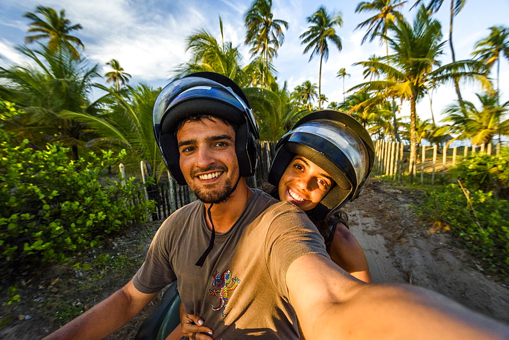 Selfie of smiling couple on quad motorcycle in Taipu de Fora beach during sunset, South Bahia near Barra Grande, Brazil