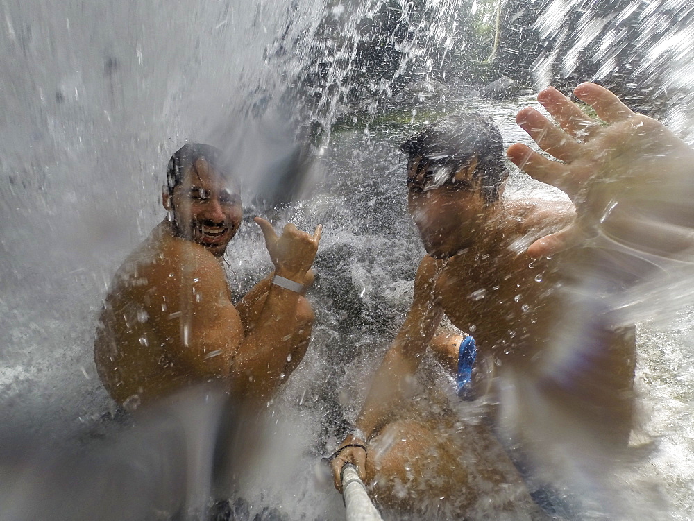 Two shirtless men taking selfie inside waterfall in Poco Verde (Green Pool), Guapimirim Sector in Serra dos Orgaos National Park, Rio de Janeiro, Brazil