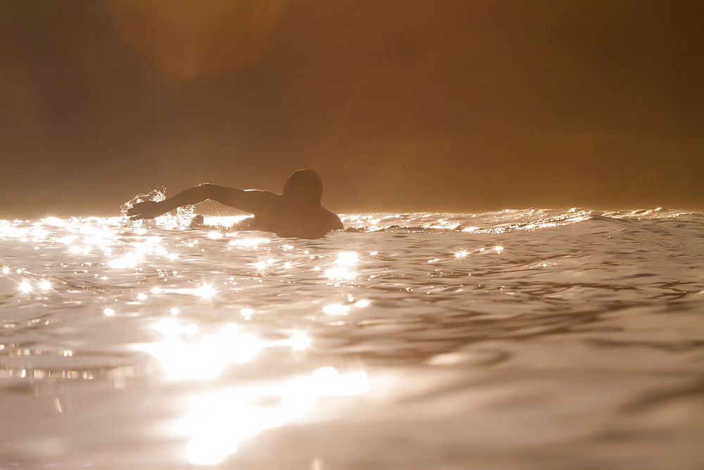 Photograph of silhouette of surfer swimming in sea at sunrise, Lakey Peak, central Subawa, Indonesia