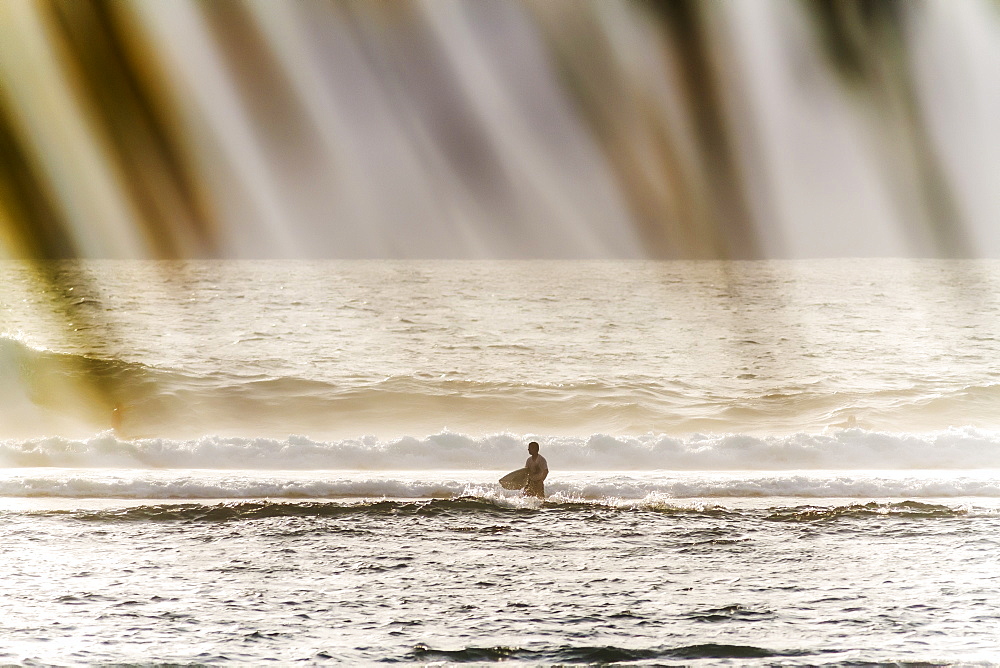 Surfer standing in sea with waves, Lakey Peak, central Sumbawa, Indonesia