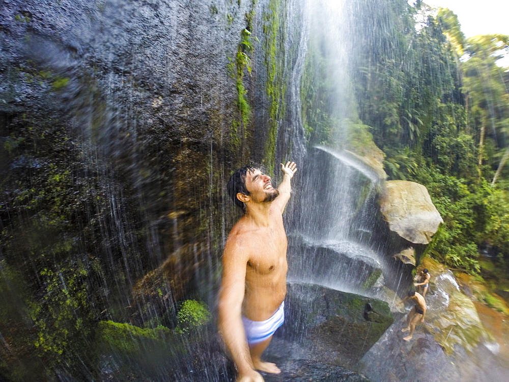 Man standing under waterfall with open arms, Guapiacu Ecological Reserve, Rio de Janeiro, Brazil