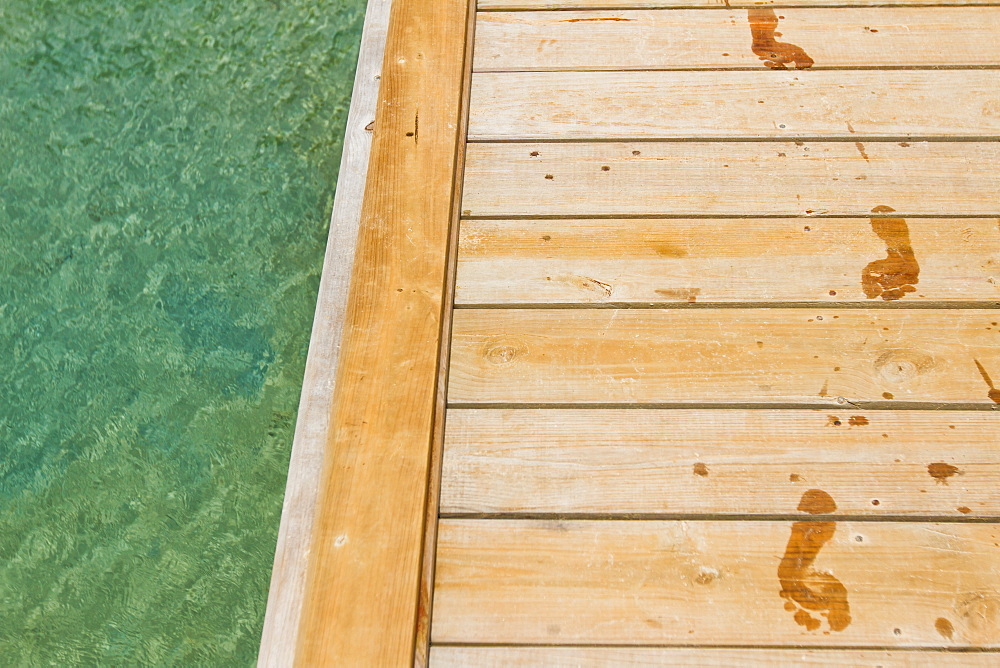 Wet footprints track on wooden pier next to sea, West End, Roatan, Honduras