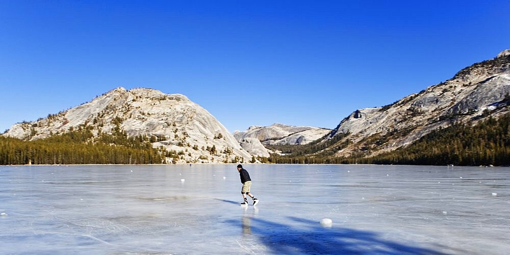A lone man ice skating on a frozen lake.