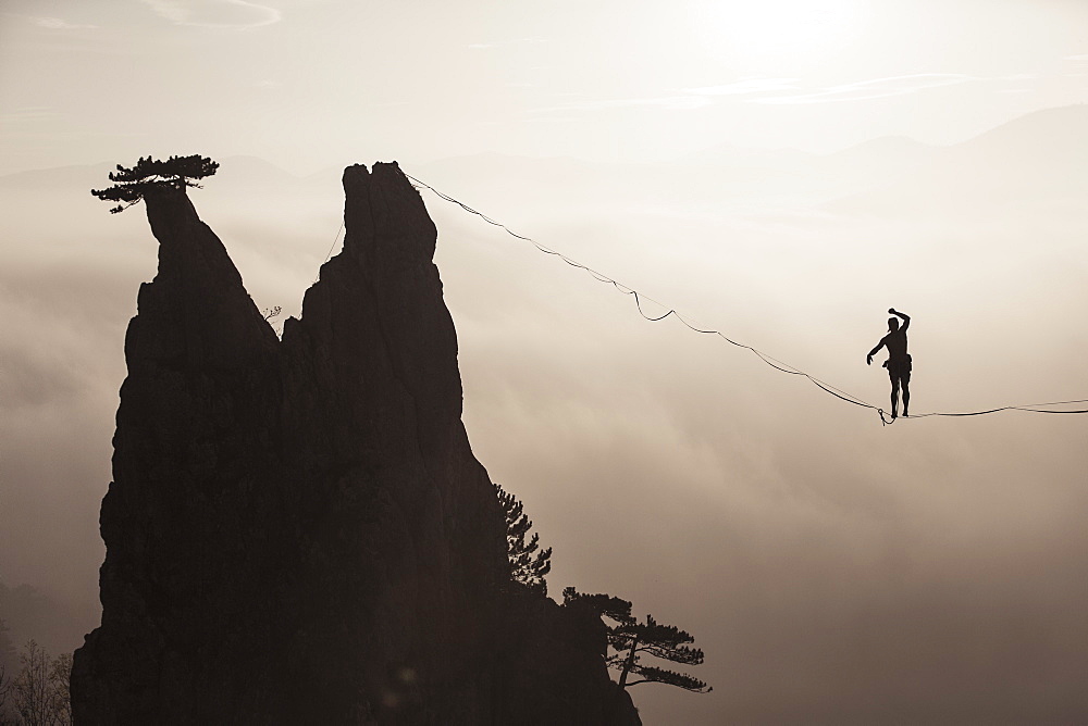 Silhouette of man balancing on highline high above foggy hills, Lower Austria, Austria