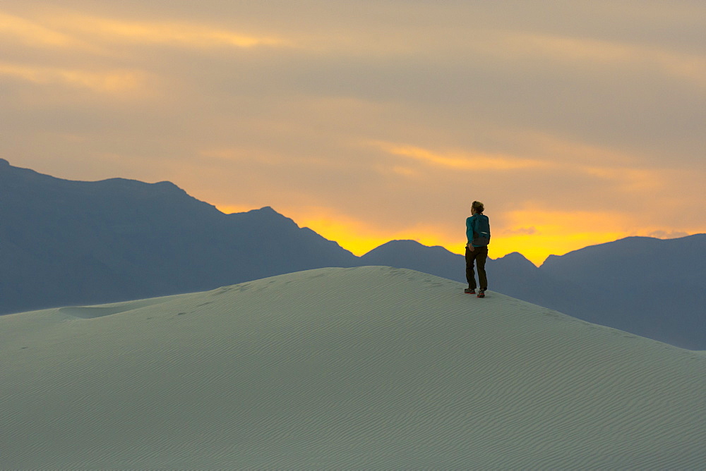 Rear view of female backpacker hiking in desert of White Sands National Monument at sunset, Alamogordo, New Mexico, USA