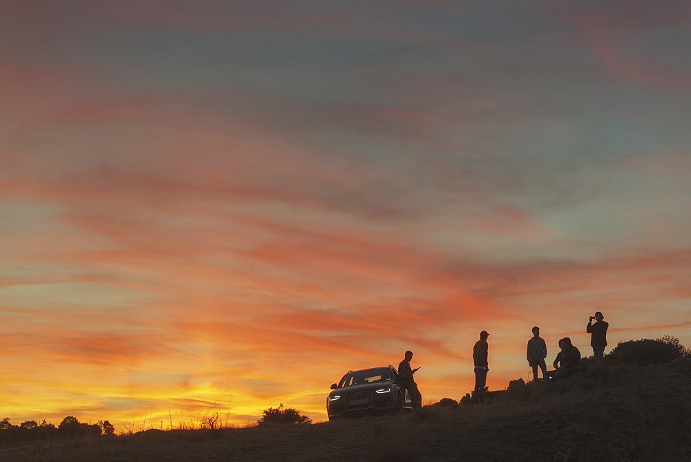 Silhouette of group of friends near car at sunset in natural setting