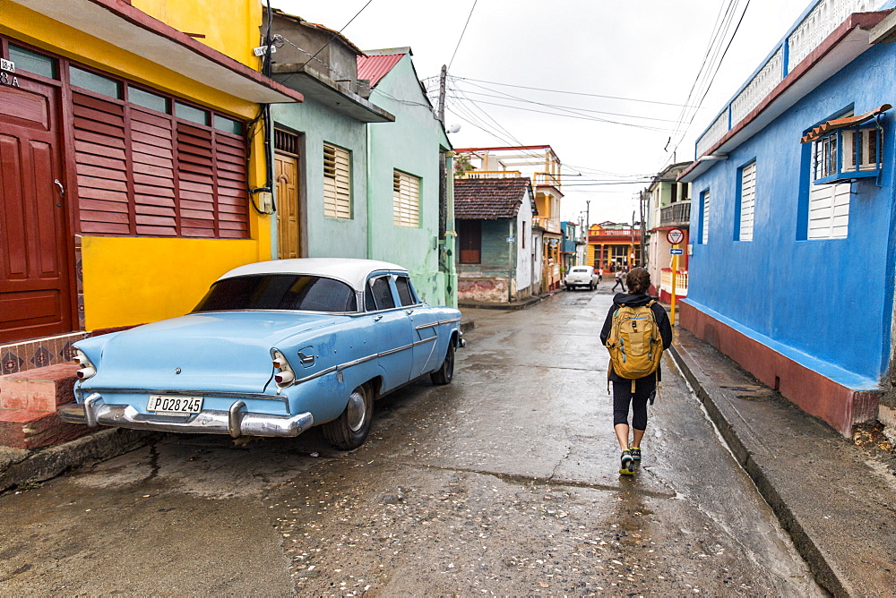 Rear view of female tourist walking on street by vintage car in Baracoa, Guantanamo Province, Cuba