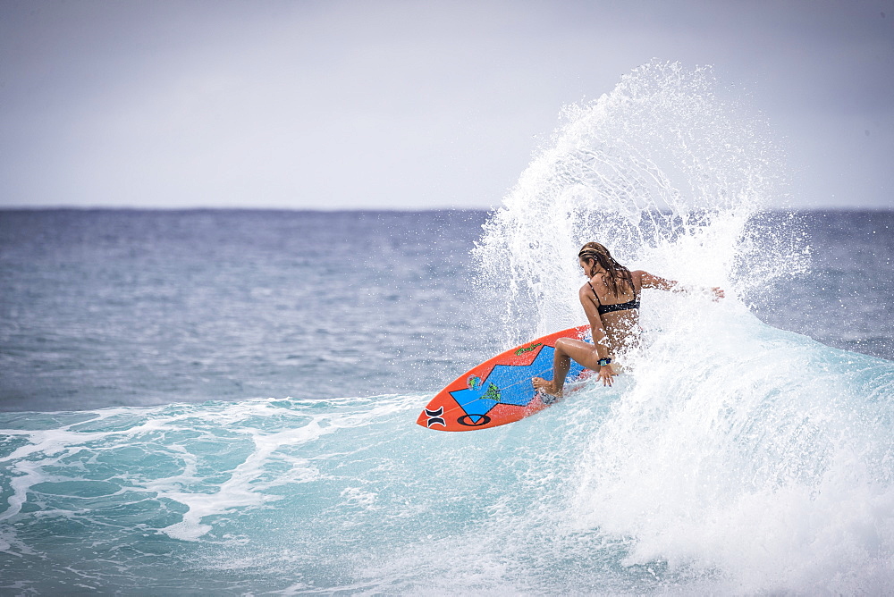 Rear view of single female surfer in bikini riding wave in sea