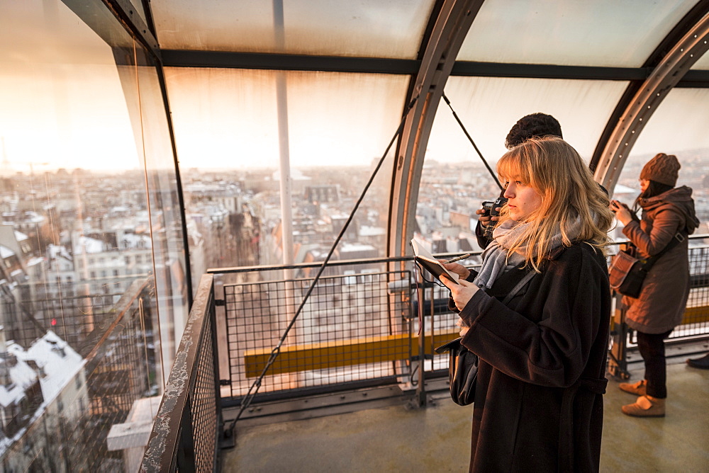 Tourists looking through window at view of Paris, France in Centre Georges Pompidou at sunset