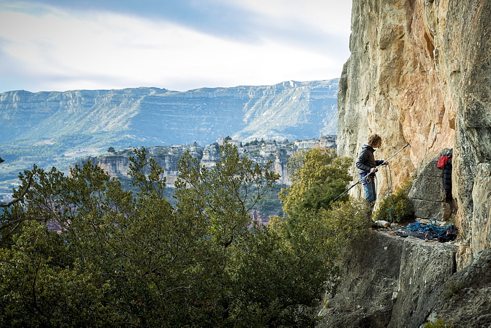 Distant view of single adventurous male rock climber preparing stick clip at cliff, Siurana, Catalonia, Spain