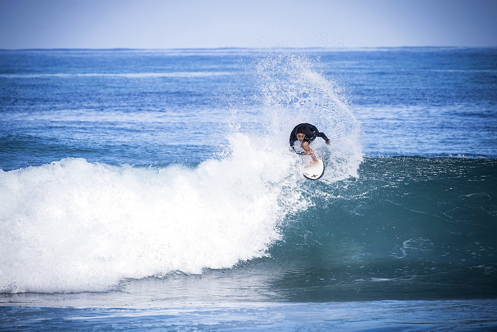 Full length shot of single boy in wetsuit surfing in sea