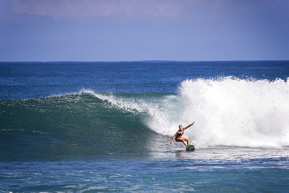 Distant view shot of single woman in bikini surfing in sea