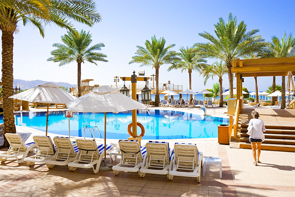 Woman walking by pool in tourist resort with palm trees, Aqaba, Jordan