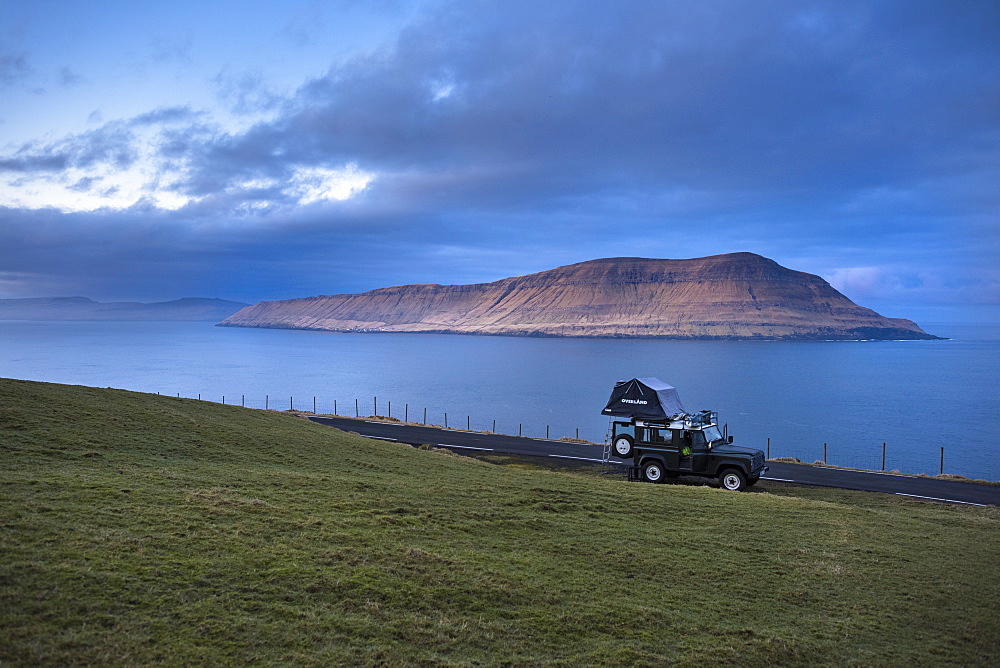 Side view of 4x4 car driving along coastline, Faroe Islands, Denmark