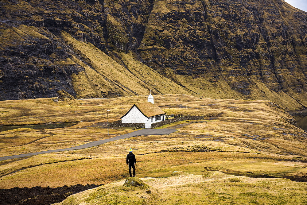 Rear view of man standing near sod roof house, Faroe Islands, Denmark