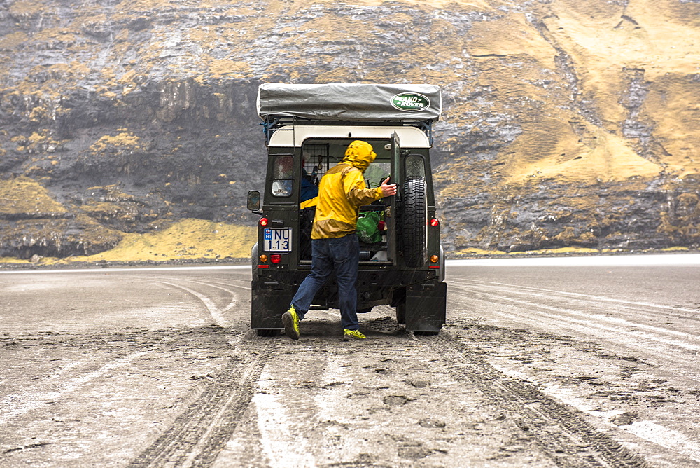 Rear view of man looking in trunk of 4x4 car in natural setting, Faroe Islands, Denmark