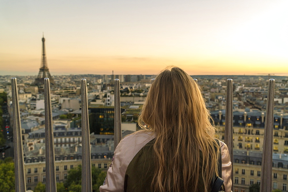 Rear view shot of single woman looking at view of Paris at sunset from Triumphal Arch, France