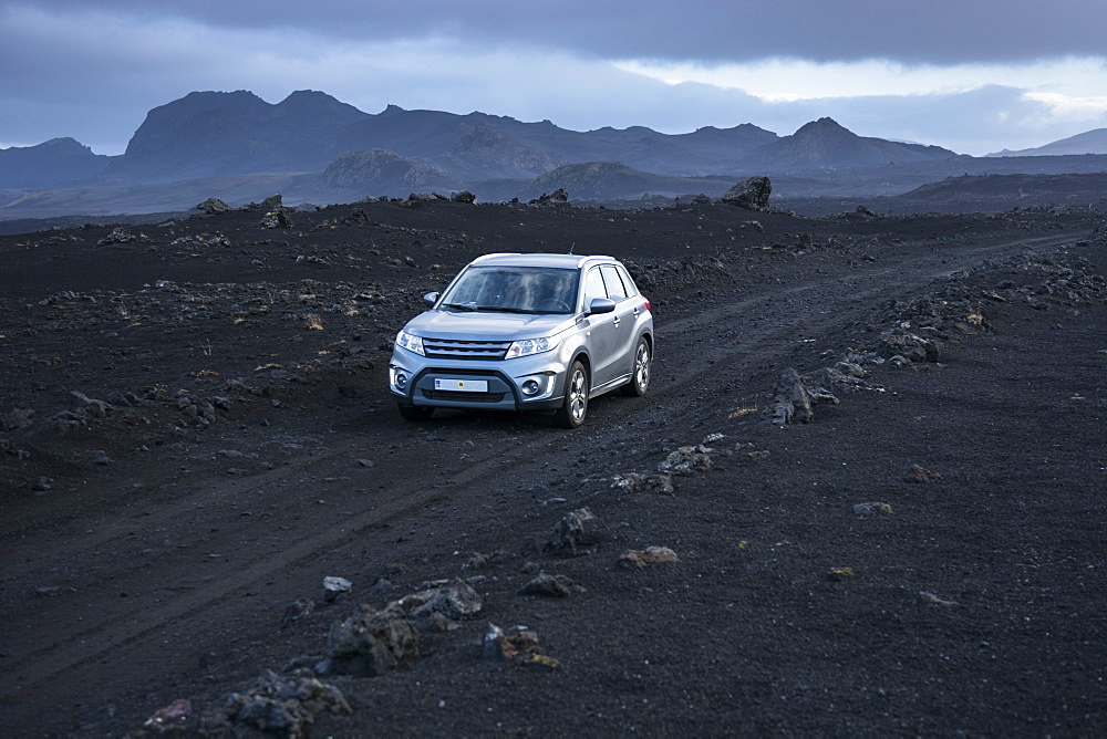 Silver-colored 4x4 SUV driving along dirt road in volcanic landscape, Sprengisandsleid, Iceland